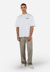 Valge lühikeste varrukatega t-särk musta tekstiga, koos heleda beeži värvi pükstega. Pükstel on sile tekstuur ja mugav lõige. Valged snikkerid lõpetavad ilme.