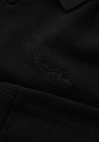 Pullover nero a maglia con colletto ripiegato, caratterizzato da un sottile logo ricamato vicino all'orlo. Tessuto morbido con polsini a coste.