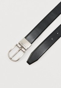 Černý kožený pásek se stříbrnou kovovou přezkou s rytím "Valentino" ležící na bílém pozadí.