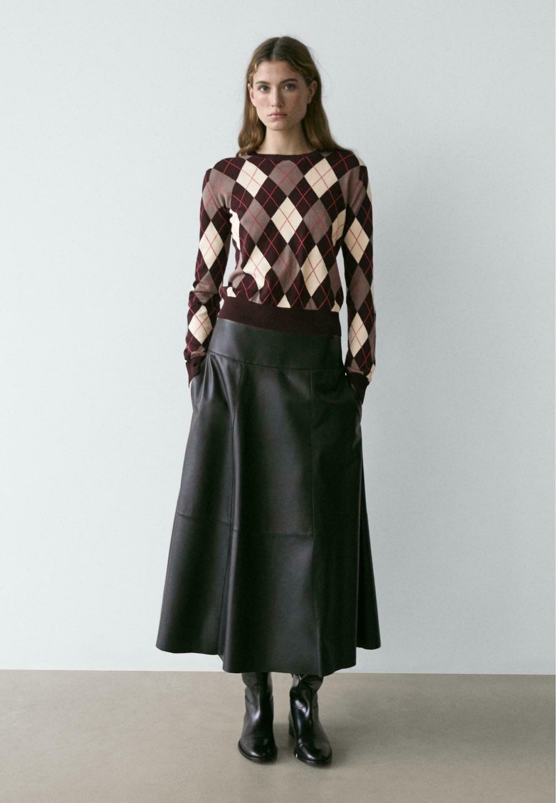 Braun-cremefarbenes Rautenmuster-Pullover mit eng anliegenden Bündchen, kombiniert mit einem langen schwarzen Lederminirock und schwarzen Stiefeletten. Glatte Texturen und geschichtetes Design.