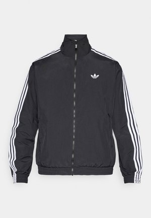 Čierna bunda na zips s vysokým golierom, s tromi bielymi pruhmi na rukávoch a malým bielym logom na hrudi. Hladká textúra látky.