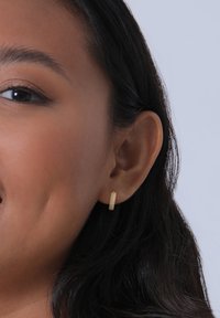 Guldörhänge i form av en ring med en texturerad yta och små diamantliknande accenter, som visar en cirkulär form och en polerad finish.