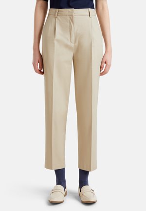 Beige tailored trousers with pleats, crafted from smooth fabric. Features a straight leg cut and high waist, paired with navy socks and loafers.