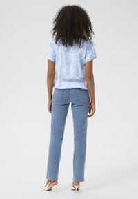 Short-sleeve blue blouse with paisley pattern, paired with light blue straight-leg jeans and beige heeled shoes, viewed from the back.