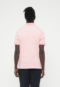 Ροζ πόλο μπλούζα με λευκές οριζόντιες ρίγες, κοντά μανίκια και γιακά. Το ύφασμα φαίνεται λείο με ελαφριά γυαλάδα.