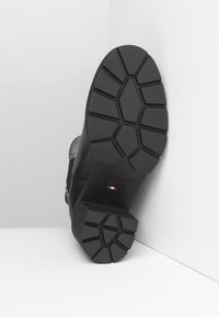 Botte en cuir noir avec une semelle en caoutchouc texturé, présentant un motif de semelle multidirectionnel et un détail de logo. Conçue pour la durabilité et l'adhérence.