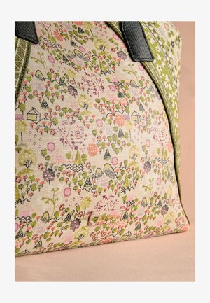 Drobės krepšys su žaliu ir rožiniu gėlių bei geometriniu raštu, juodos rankenos ir nedideliu stačiakampio formos prekės ženklo etiketė ant audinio paviršiaus.