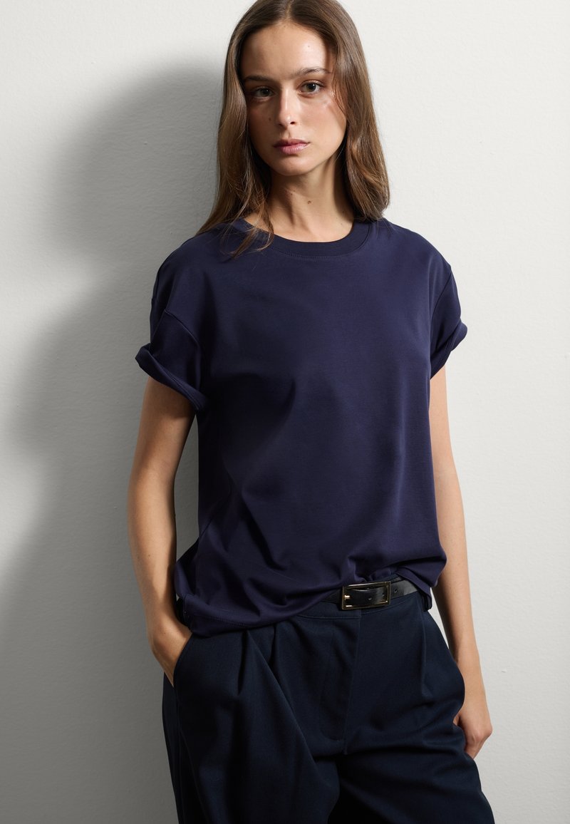 Maglietta blu navy a maniche corte con risvolti, realizzata in tessuto morbido, abbinata a pantaloni scuri e una cintura nera. Design semplice e classico.