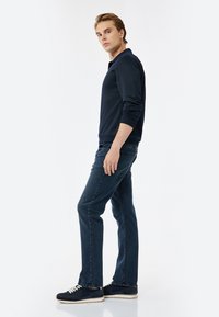 Sudadera navy de manga larga, combinada con unos vaqueros azul oscuro y zapatillas navy. El conjunto tiene un corte relajado y un diseño sencillo.