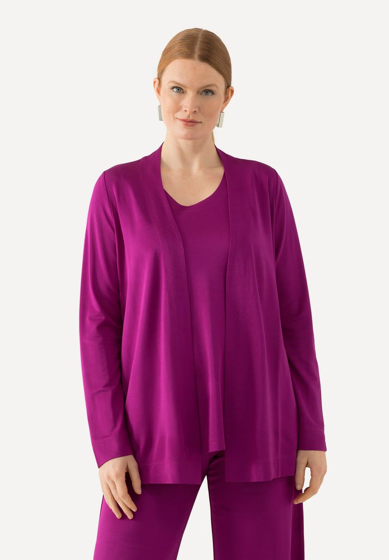 Lila Strickjacke aus weichem Material, offenes Vorderdesign, lange Ärmel, kombiniert mit einem passenden Oberteil, getragen über strukturierten lila Hosen.