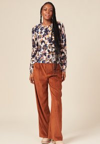 Maglione floreale a maniche lunghe di colore crema, con tonalità di blu e arancione, abbinato a pantaloni a gamba larga in corduroy color ruggine.