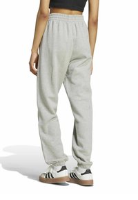 Sivé tepláky s elastickým pásom, s manžetami na členkoch a mäkkou textúrou, kombinované s bielo-čiernymi teniskami s hnedou podrážkou.