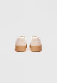 Sneaker bianchi con retro in suede, design arrotondato e suola in gomma. Lacci semplici e dettagli di cucitura minimalisti.