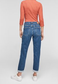 Blaue Denim-Jeans mit geradem Bein, umgekrempelten Säumen und zwei hinteren Taschen. Kombiniert mit einem orangefarbenen Rippoberteil und weißen Sneakers.