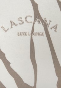 Top de loungewear con una base color crema y un patrón abstracto marrón. El texto bordado dice "LASCANA LUXE LOUNGE". Textura suave.