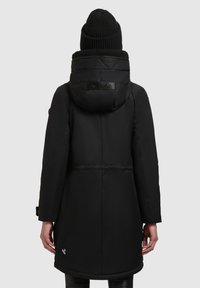 Zwarte gewatteerde jas met een doorgestikte capuchon, faux fur voering en een logo patch. Heeft lange mouwen en een rechte snit, die tot halverwege de bovenbenen reikt.