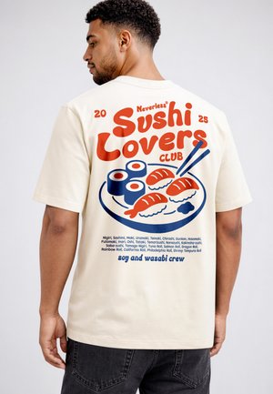 Mann trägt cremefarbenes T-Shirt mit roter und blauer Sushi-Illustration und dem Schriftzug „Sushi Lovers Club“ auf dem Rücken.