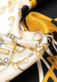Écharpe en soie présentant un design noir, blanc et or avec des motifs intricats d'instruments de musique, texture lisse et un léger éclat.