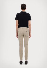 Czarna koszulka polo i dopasowane beżowe spodnie. Spodnie mają dwie tylne kieszenie zapinane na guziki. Gładka tkanina z lekkim rozciągnięciem.