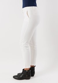 Jeans bianchi elasticizzati con un design aderente, due tasche laterali e una tasca posteriore, abbinati a stivaletti neri alla caviglia con cerniere.