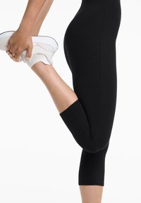 Legginguri negre scurte dintr-un material elastic, cu o textură netedă și un design ajustat, asociate cu teniși albaștri sport.