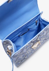 Sac à main à motif floral bleu avec un fermoir doré, doté d'un intérieur bleu clair, d'une poche zippée et d'un extérieur en tissu texturé.