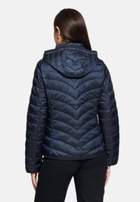 Doudoune bleu marine avec un motif matelassé en chevrons, capuche, texture brillante et poignets élastiques, vue de dos.