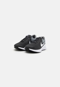 Baskets athlétiques noires avec un dessus en maille, des accents gris, une semelle blanche et un grand logo swoosh sur le côté. Présente un design à lacets.