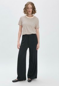 Raidallinen pyöreäkauluksinen t-paita beige- ja ruskeasävyissä, yhdistetty laajarajaisiin mustiin housuihin, jotka on valmistettu pehmeästä kankaasta. Litteät mustat kengät viimeistelevät asustuksen.