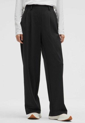 Pantalones de pierna ancha con raya diplomática negra, combinados con zapatillas blancas y una camiseta blanca de manga larga, mostrados desde la cintura hasta los pies.