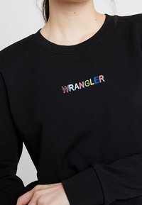 Felpa nera con logo "WRANGLER" multicolore sul petto, scollo tondo e maniche lunghe. Tessuto in cotone morbido.