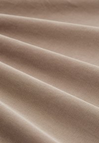 Beige stof met een getextureerd, geribbeld oppervlak, in zachte plooien gerangschikt, waarbij gladde lijnen en een subtiele glans worden getoond.