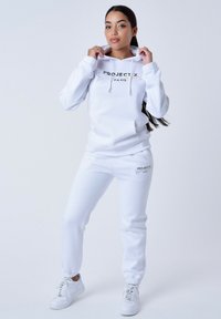 Witte katoenen hoodie met een voorzak en trekkoorden; gecombineerd met bijpassende joggers, voorzien van een kleurrijke "PROJECT X PARIS" logo aan de zijkant.