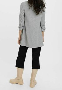 Szara tunika z długim rękawem o luźnym kroju i podwiniętych rękawach, zestawiona z czarnymi spodniami typu wide-leg oraz beżowymi kozakiem sięgającymi do kolan.