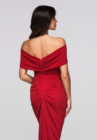 Czerwona sukienka wieczorowa z odkrytymi ramionami, wykonana z błyszczącego materiału. Posiada marszczenia z tyłu oraz dopasowaną sylwetkę.