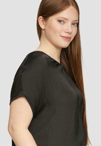 Schwarzes kurzärmeliges Oberteil mit V-Ausschnitt und glatter Textur. Verfügt über eine lockere Passform und einen dezenten Glanz. Einfacher, minimalistischer Stil.
