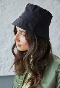 Chapéu bucket preto feito de tecido, com um design liso, textura suave, aba larga e uma construção de duas painéis.