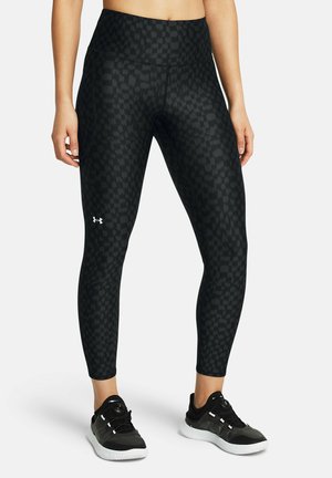 Black leggings with a checkered pattern, high waistband, and stretch fabric, paired with black athletic shoes. Under Armour logo visible.