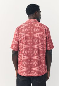 Camicia a maniche corte rossa con motivi geometrici e vestibilità rilassata. Realizzata in tessuto strutturato con colletto.