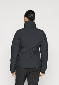 Sort pufferjakke med høj krave, diamantquiltet mønster og elastiske manchetter. Stoffet ser slidstærkt og isoleret ud til varme.