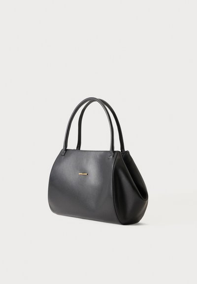Sac à main en cuir noir avec deux poignées et un petit détail horizontal en barre dorée à l'avant, sur un fond clair uni.