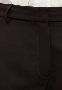 Σκούρο καφέ παντελόνια με ομαλή υφή, ραμμένη σχεδίαση, μπροστινές τσέπες και θηλιά για ζώνη στη μέση. Ορατή λεπτομέρεια με ανοιχτό χρώμα στο ράψιμο.