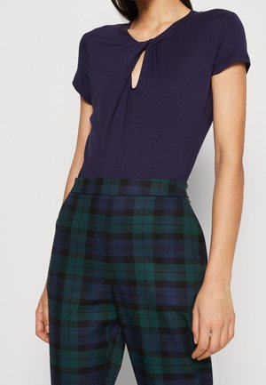 Mørkeblå kortærmet top med en nøglehulsdesign ved halsen, parret med grøn- og sortternet, højtaljede bukser med flad front.