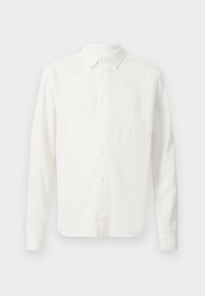 Bela srajca z dolgimi rokavi iz teksturirane tkanine, s kravato z gumbi in sprednjim zapiranjem na gumbe. Ima običajen kroj in gladek, enostaven dizajn.