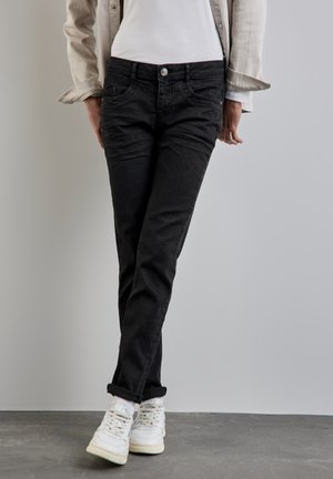 Black denim jeans with a slim fit, featuring front pockets, a button closure, and rolled cuffs, paired with white sneakers.