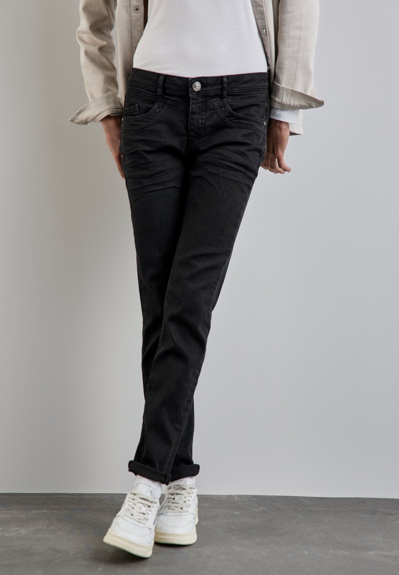 Svarta jeans i slim fit med framfickor, knäppning och uppvikta benslutar, tillsammans med vita sneakers.