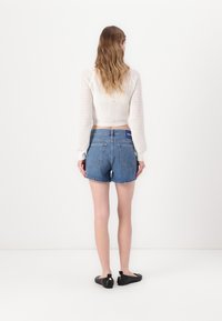 Suéter corto blanco de punto con mangas largas, combinado con pantalones cortos de mezclilla deslavados con dobladillo sin terminar y dos bolsillos traseros. Zapatos planos negros.