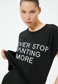Sort, kortærmet top med en løs pasform. Har hvid tekst med teksten "NEVER STOP WANTING MORE" centreret på forsiden. Blød tekstur.