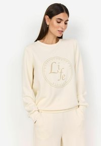 Crème-kleurige sweatshirt met lange mouwen, ronde halslijn en een centraal textuurgraphic met de tekst "Dankbaar, Waarderend, Leven, Gezegend."