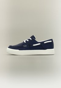 Παντόφλα σκάφους σε ναυτικό μπλε με λευκά κορδόνια, λευκές πλευρικές τρύπες, λευκή σόλα και αντίθετο λευκό ράψιμο σε ουδέτερο φόντο.